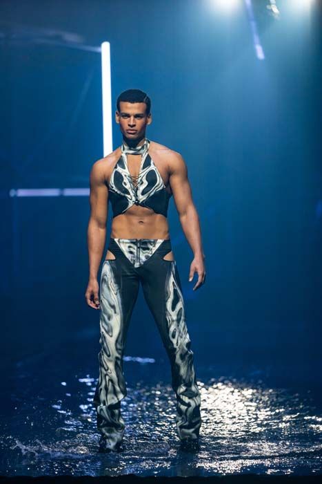 Boureima trägt ein gewagtes Outfit, das seine Muskeln zur Schau stellt.